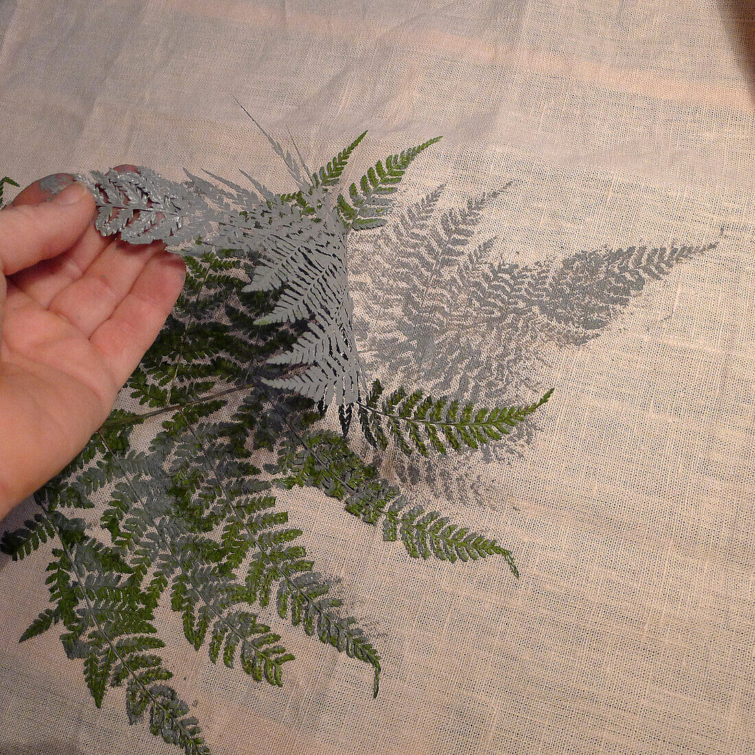 Hand peeling a painted fern leaf off printed fabric