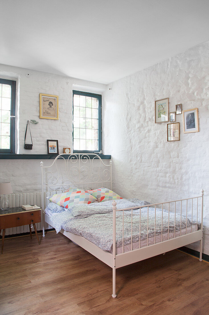Metal bed in bedroom with whitewashed stone walls and lattice windows