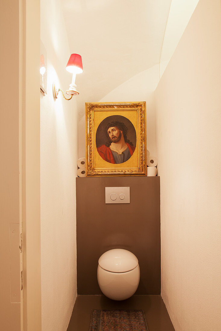 Picture of Jesus in gilt frame on ledge above round toilet