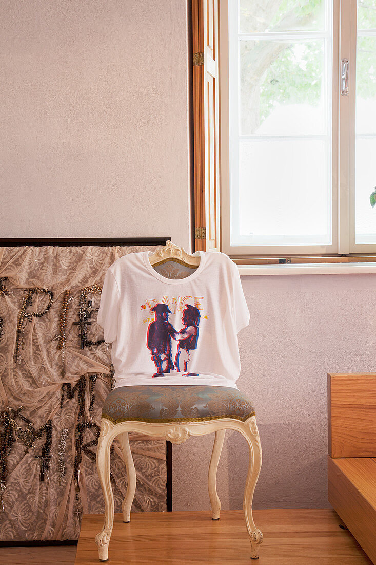 T-Shirt über der Lehne eines alten Barockstuhls vor dem Fenster