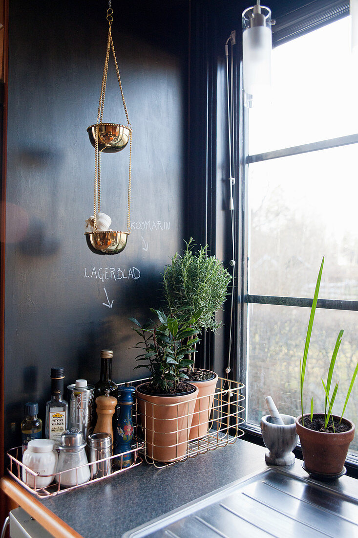 Wire baskets and golden hanging bowls in kitchen with black wall
