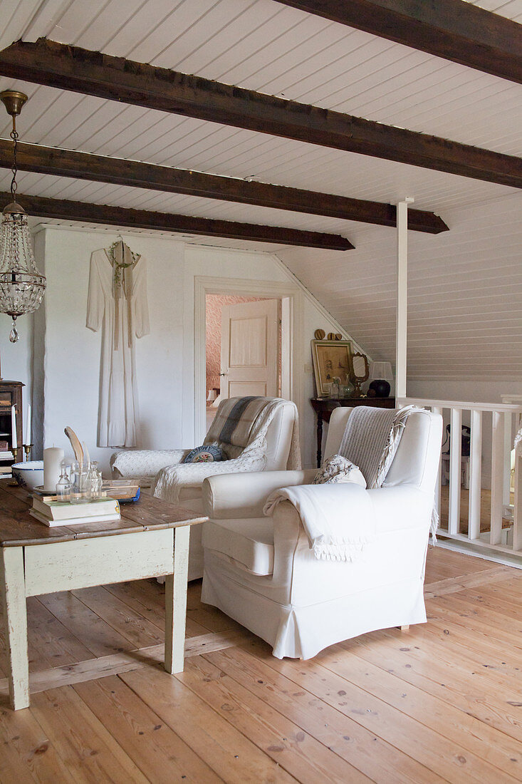 Two white armchairs in rustic living room with wooden roof beams and sloping wall