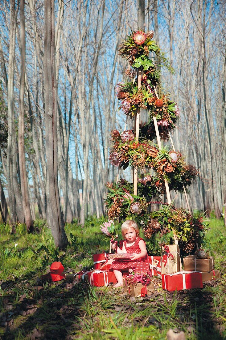 Stilisierter Weihnachtsbaum mit Proteablüten und sitzendem Mädchen im kahlen Wald