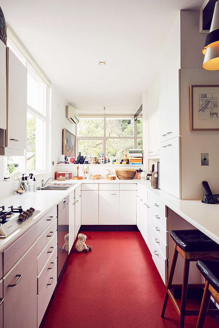 weiße Unterschränke und Frühstückstheke in schmaler Küche mit rotem Boden