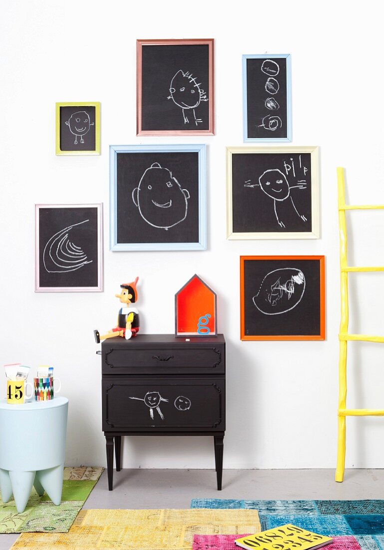 Bunt gerahmte schwarze Tafeln mit Kinderzeichnungen an weißer Wand
