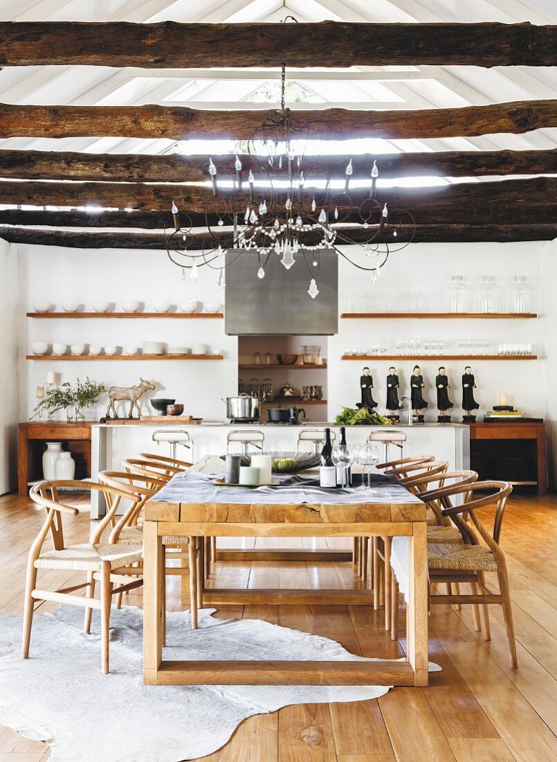 Essbereich mit Klassikerstühlen und rustikalen Holzbalken vor offener Küche