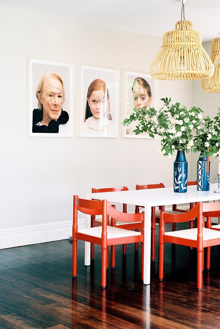 Portraitfotos über dem Esstisch mit roten Stühlen und Blumen