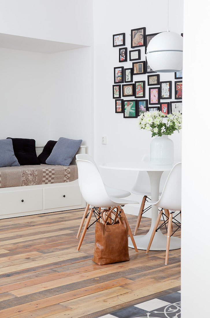 Designerstühle am runden Esstisch vorm Tagesbett und der Bilderwand
