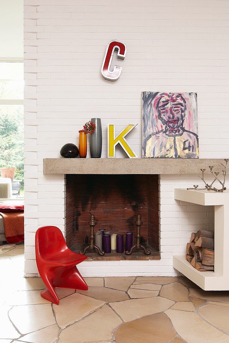 Red classic chair next to candles and candlesticks in open fireplace