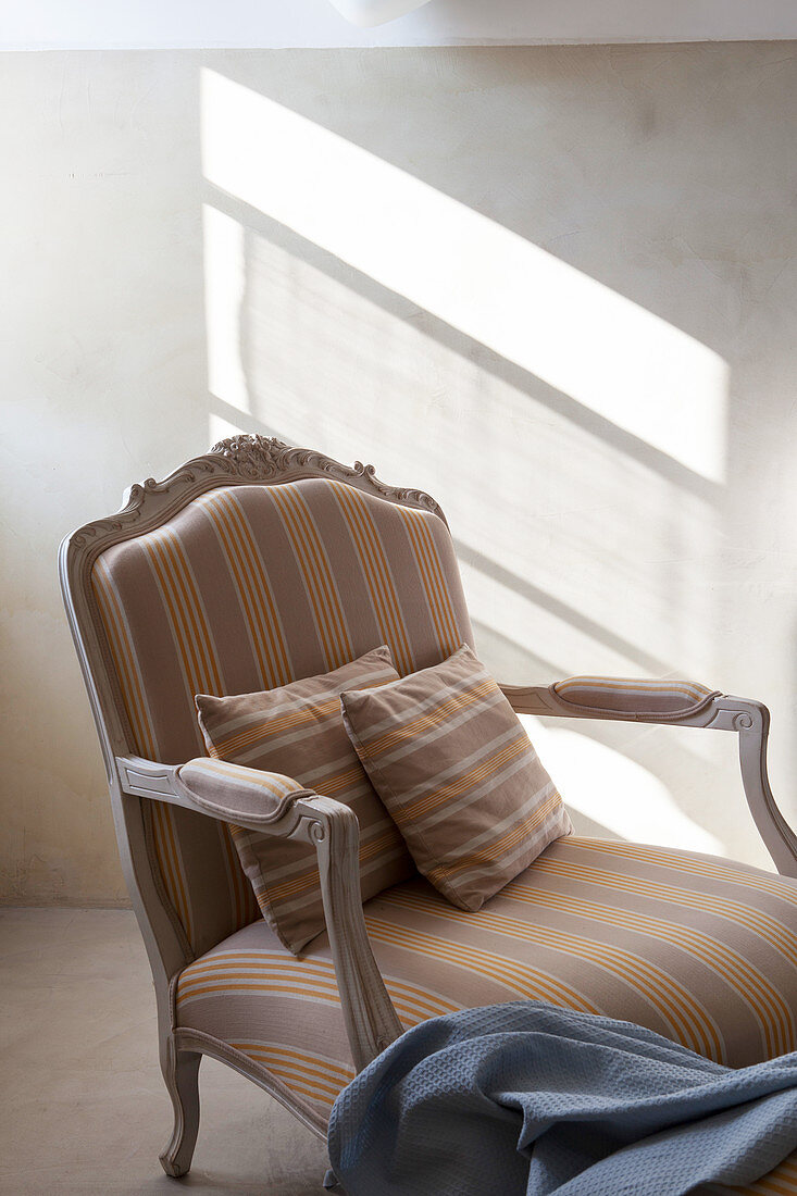 Striped scatter cushions on striped Baroque armchair in slanting sunshine