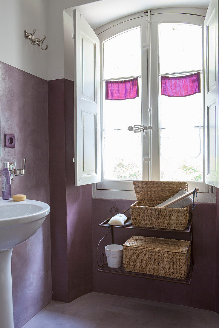 Wandregal mit Körben unterm Fenster im Bad mit violetten Wänden