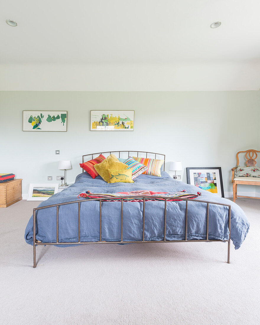Colourful scatter cushions on metal bed against pale green bedroom wall