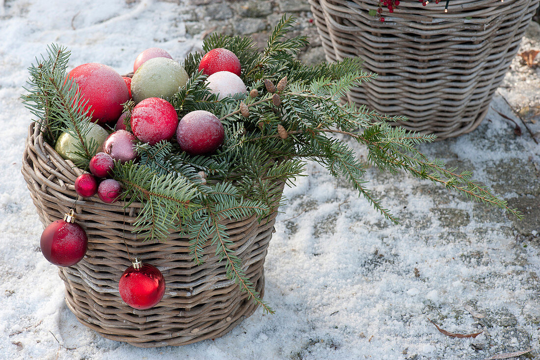 Basket with conifer branches and Christmas baubles, snow