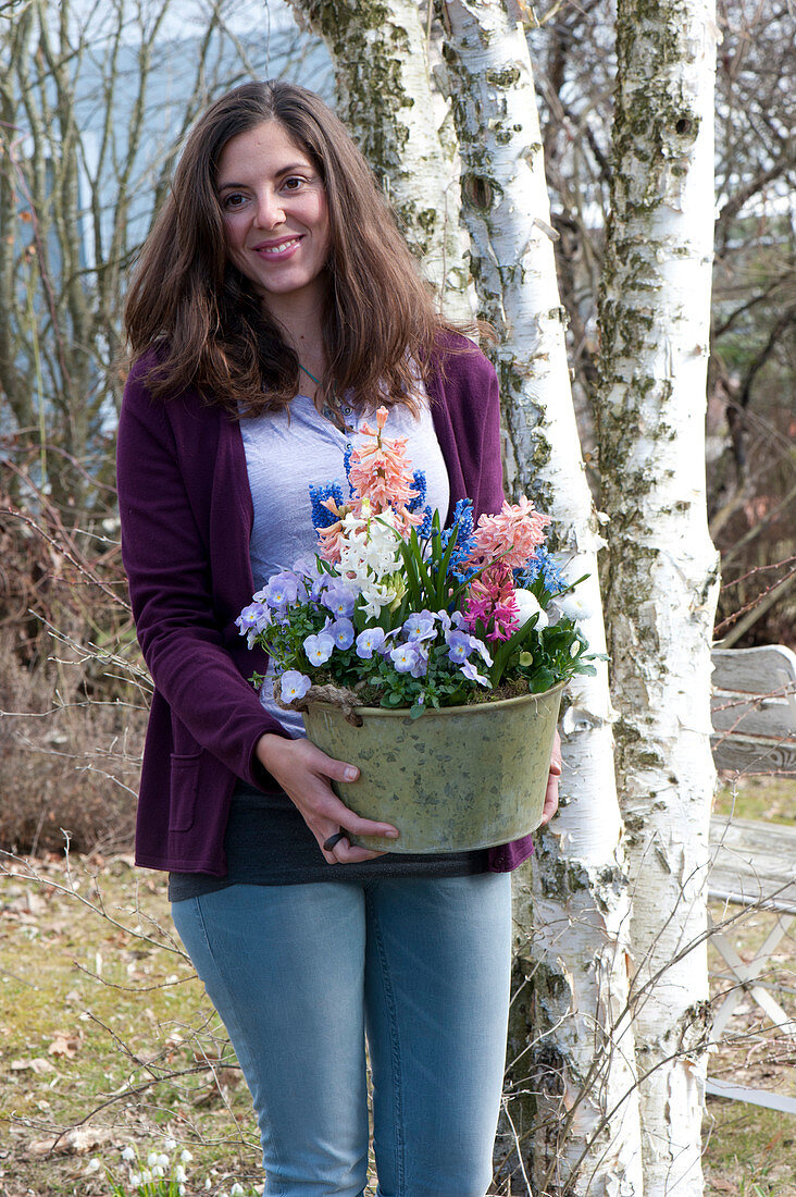 Woman bringing pot with Hyacinthus, Viola cornuta 'Lavender Blush'
