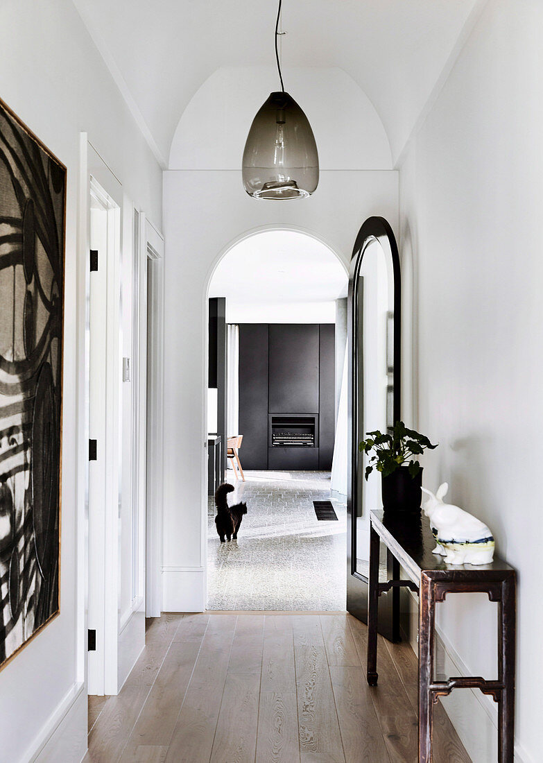 White hallway with antique console table and pendant lamp, open arched door to living room