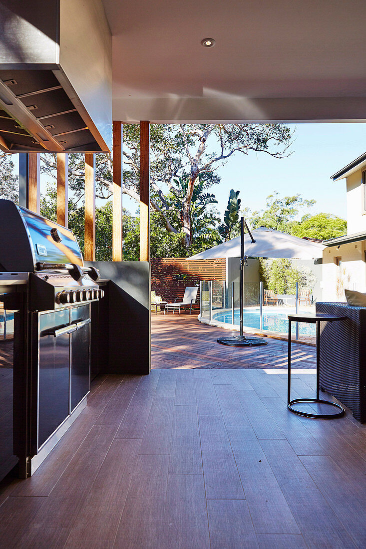 Überdachte Terrasse mit Outdoor-Küche, im Hintergrund Pool