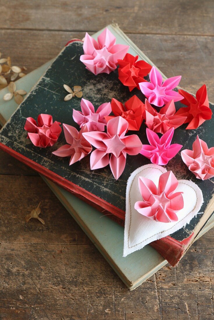 Origami flowers in various shades of red and pink on old books