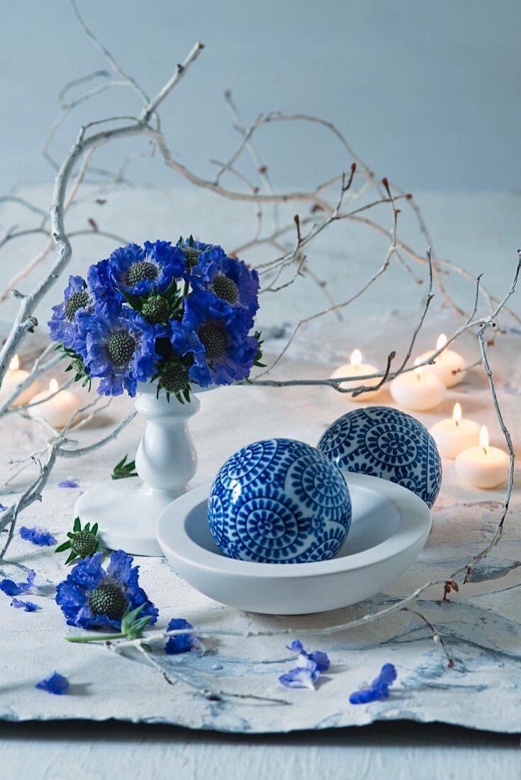 Posy of blue flowers next to white branch and ornamental spheres