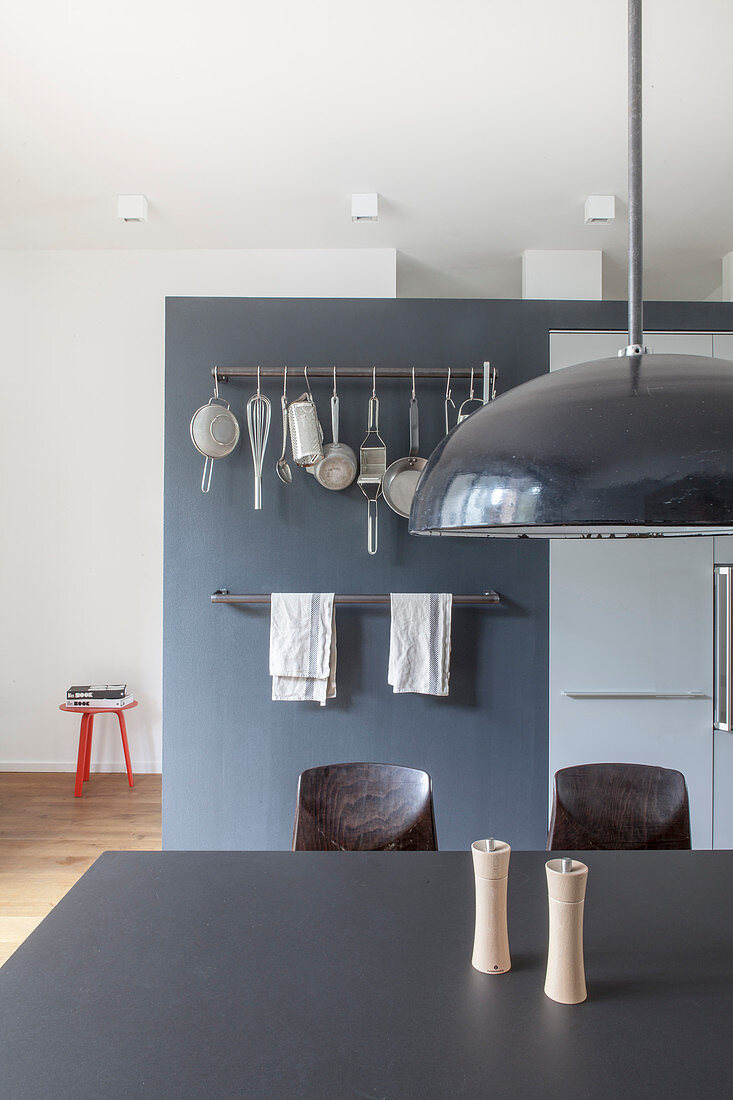 Schwarzer Tisch in offener Küche vor grauer Wand mit Hakenstangen