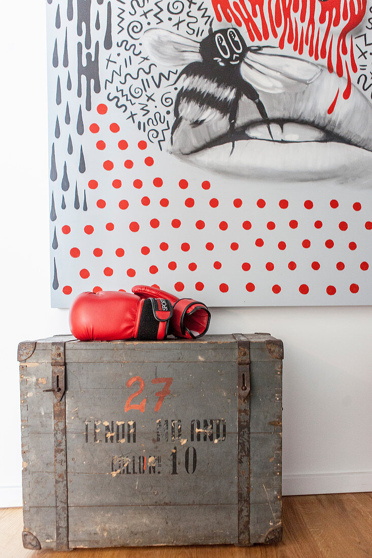 Rote Boxhandschuhe auf einer alten Holzkiste vor modernem Gemälde