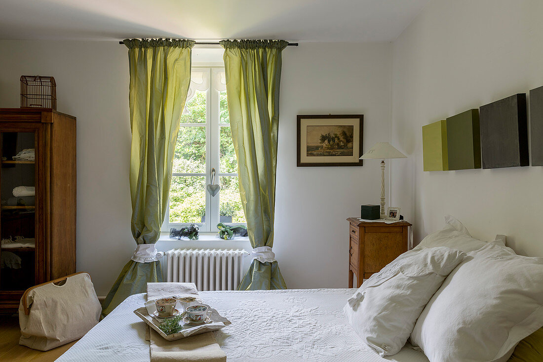 Doppelbett mit Frühstückstablett und antiker Nachtschrank in rustikalem Schlafzimmer mit grünem Vorhang