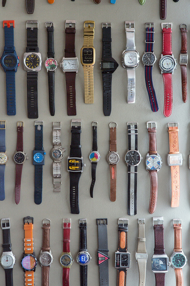 Sammlung von Armbanduhren hängt in Reihen an grauer Wand