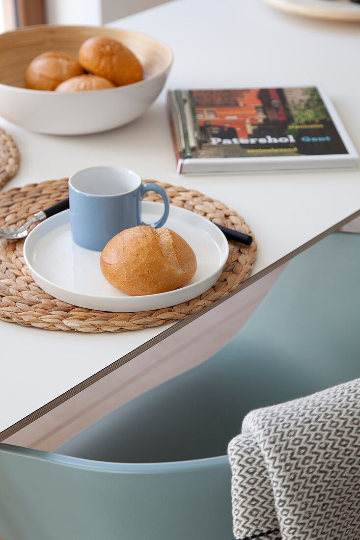 Blue mug and bread roll on raffia place mat on breakfast table