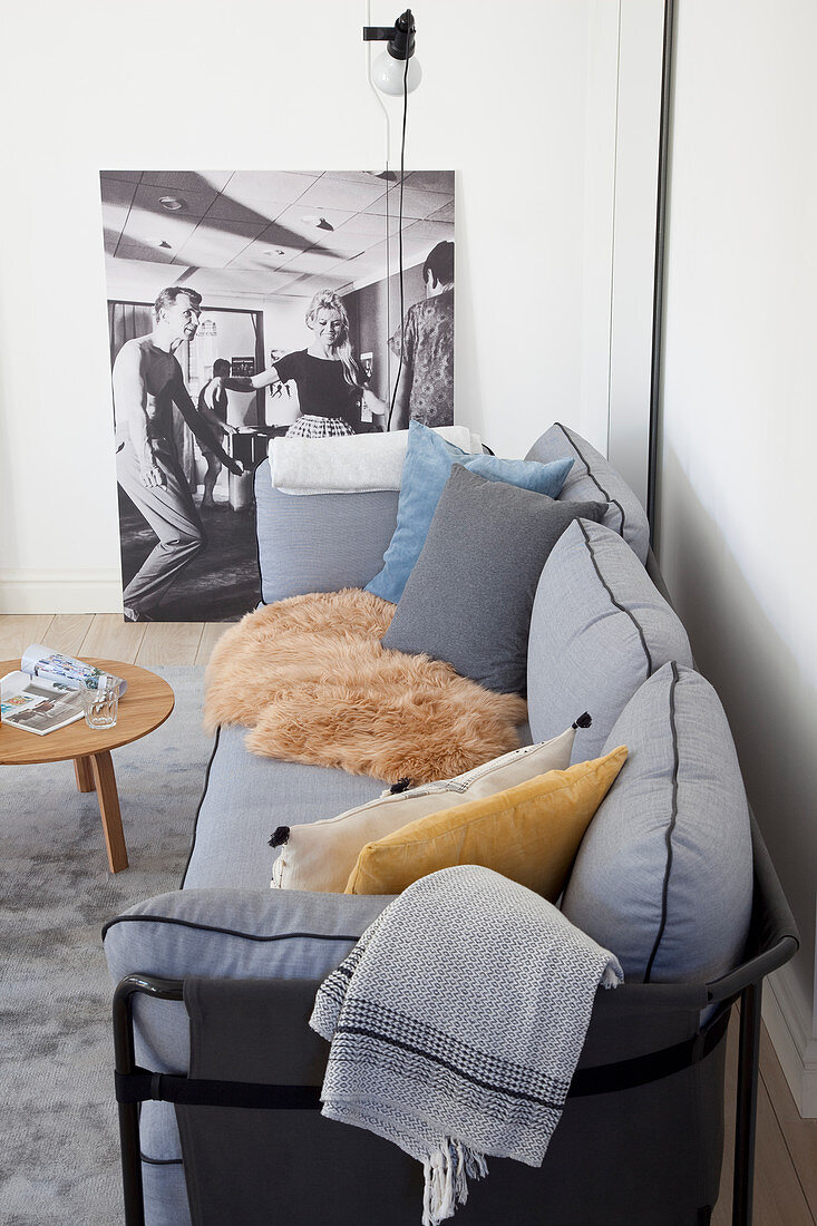 Cushions and fur rug on grey sofa in front of large photo in living room