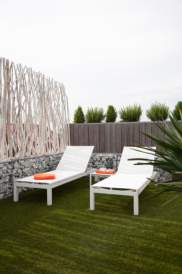 Two white loungers next to screen made from branches and gabions