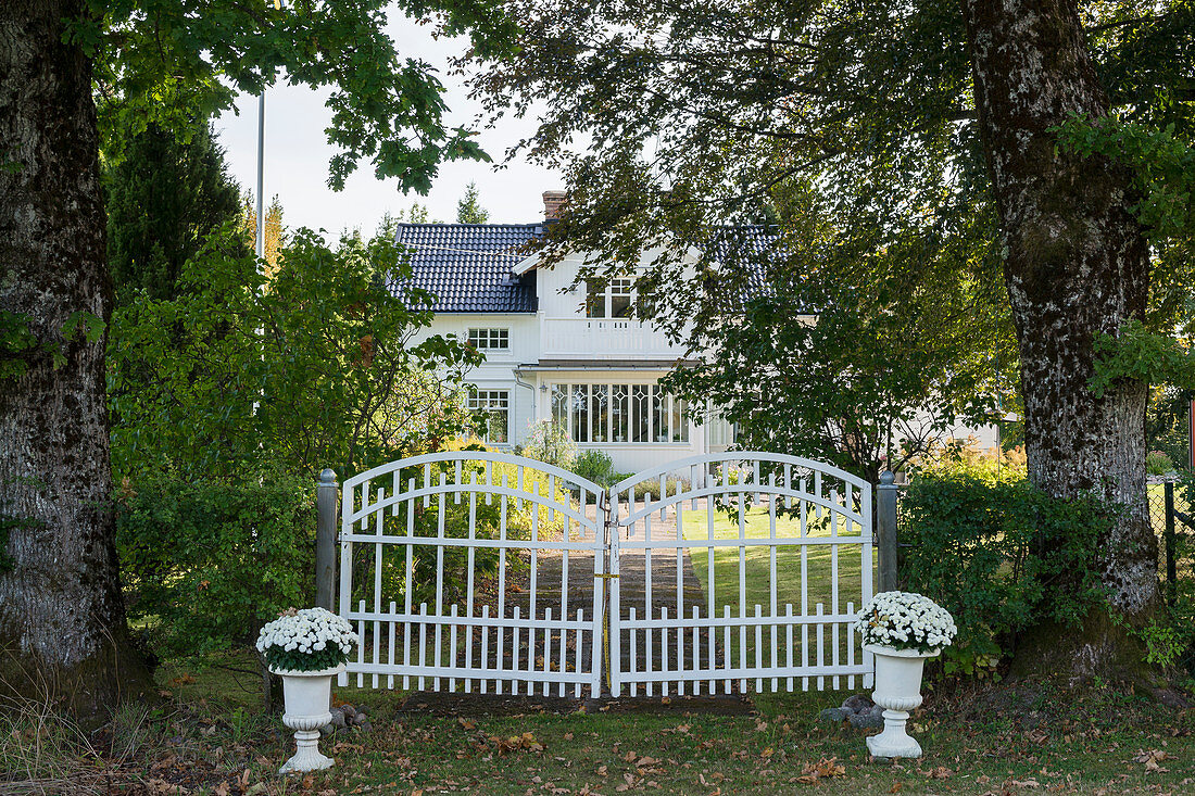 Tor zur Einfahrt eines weißen Schwedenhauses im Wäldchen