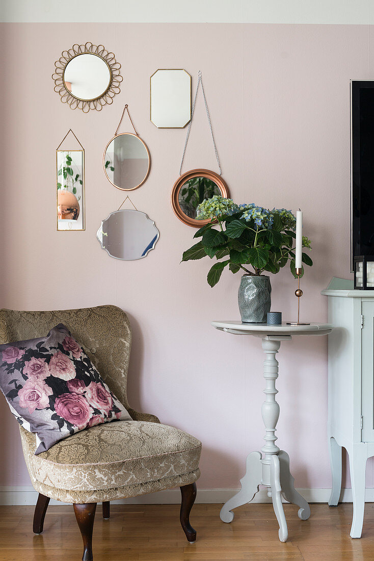 Alter Sessel vor rosafarbener Wand mit Spiegelsammlung