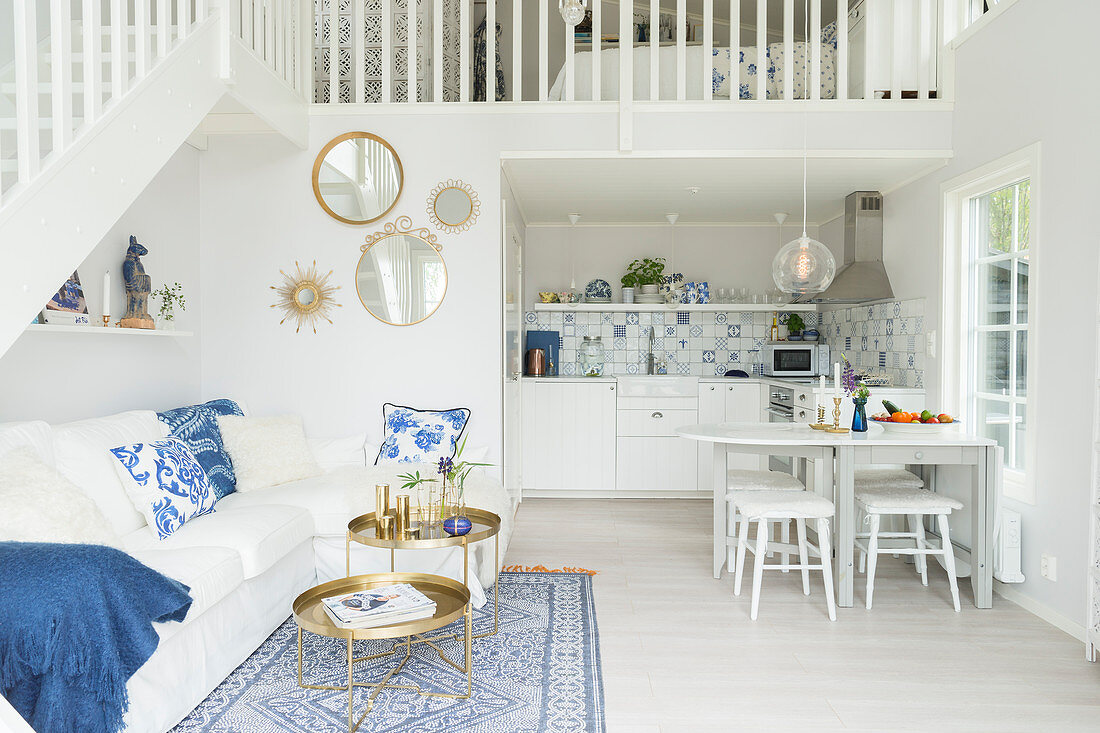 White couch, white dining table and kitchen below gallery in open-plan interior