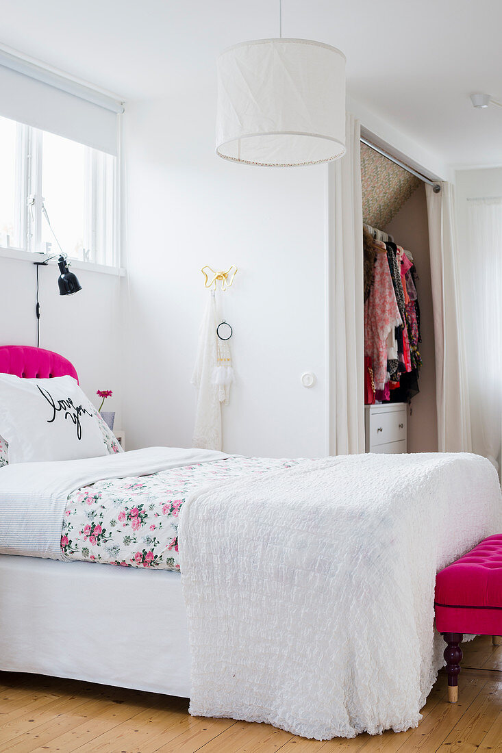 Doppelbett in weißem Schlafzimmer mit pinkfarbenen Akzenten, begehbarer Kleiderschrank hinter Vorhang
