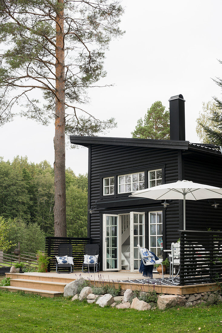Holzhaus mit Pultdach und Sprossentüren, Terrasse mit Sonnenschirm