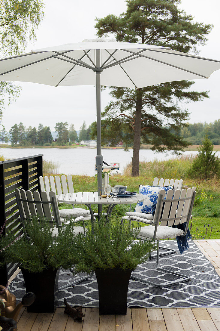 Runder Tisch mit Sonnenschirm und Stühlen auf Terrasse mit Seeblick