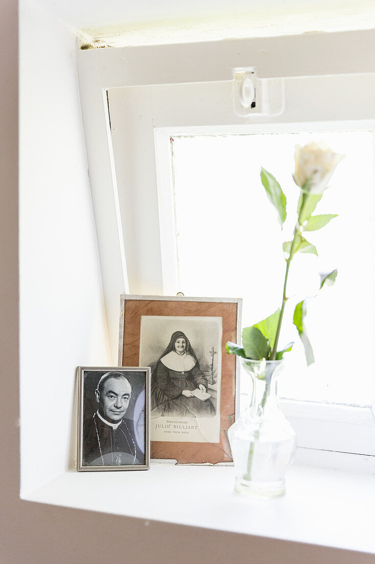 weiße Rose und Fotos von einem Priester und einer Nonne im Fenster
