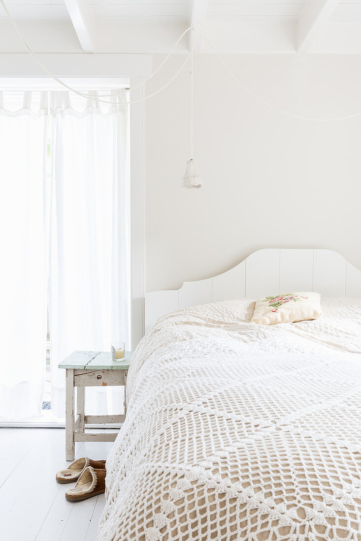 Spitzendecke auf dem Bett im hellen Schlafzimmer ganz in Weiß