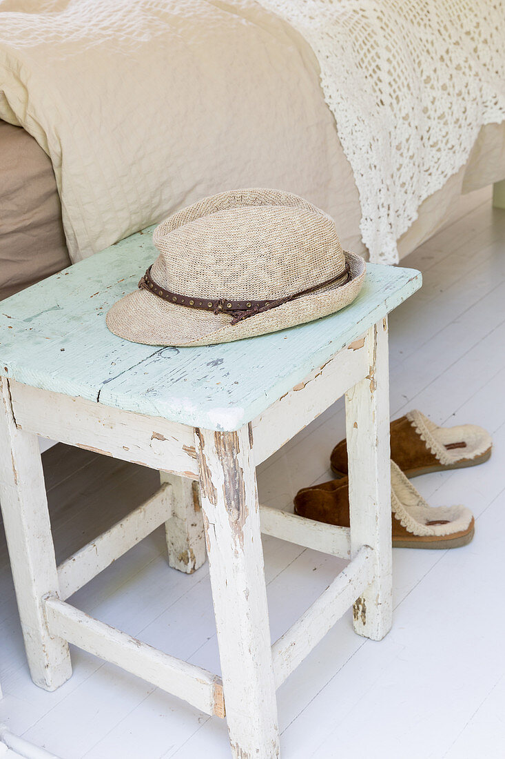 Summer hat on old stool with peeling paint next to bed