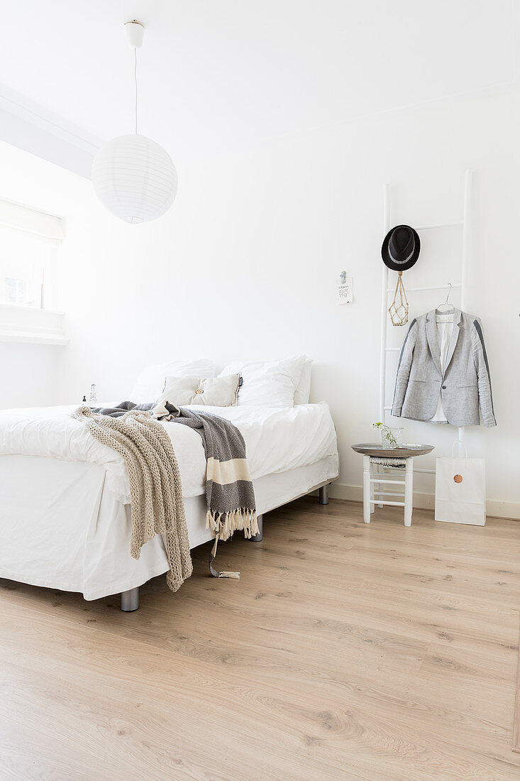 Doppelbett und Leiter als Kleiderständer in weißem Schlafzimmer mit Holzdielenboden