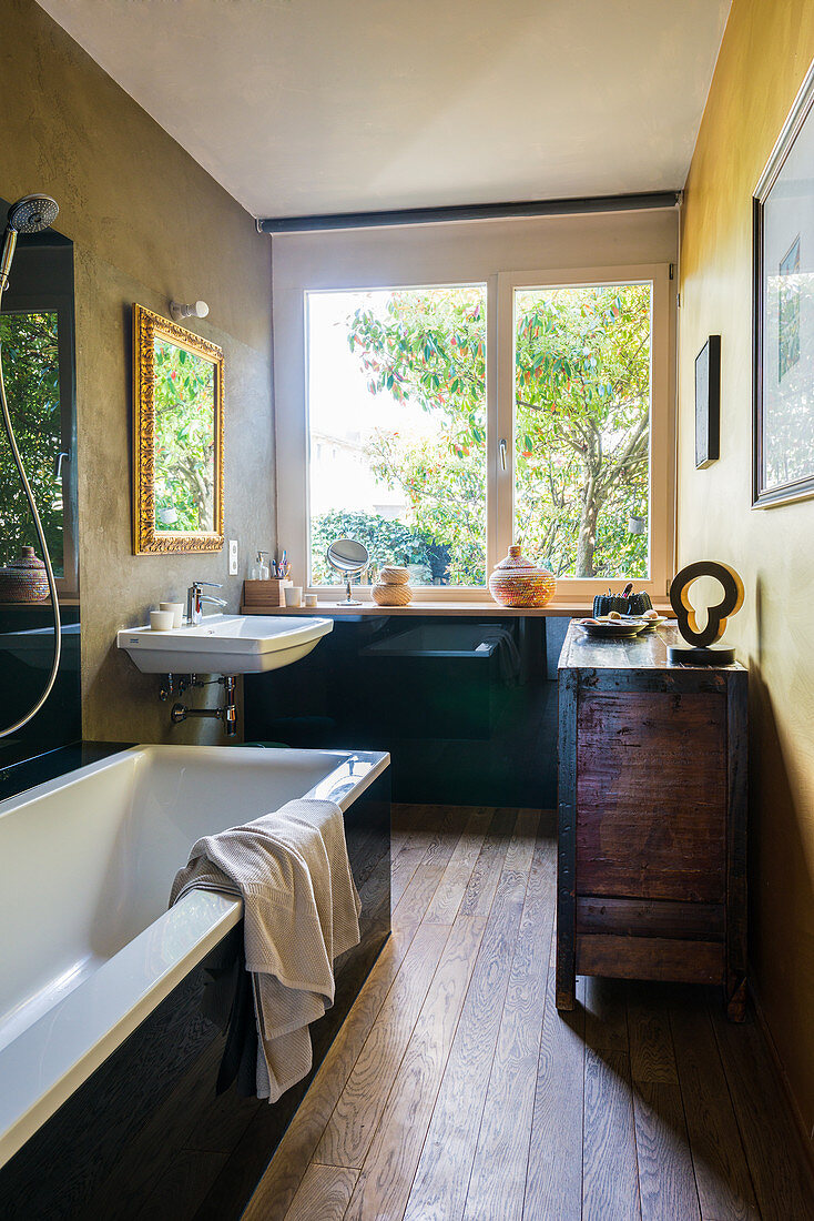 Badewanne, antik Kommode und Waschbecken im Badezimmer mit Fenster und Holzdielenboden