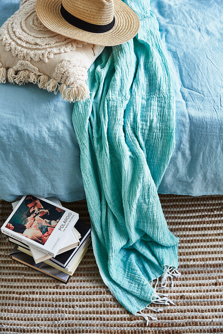 Sommerhut, Kissen und Schal auf dem Bett, daneben ein Bücherstapel