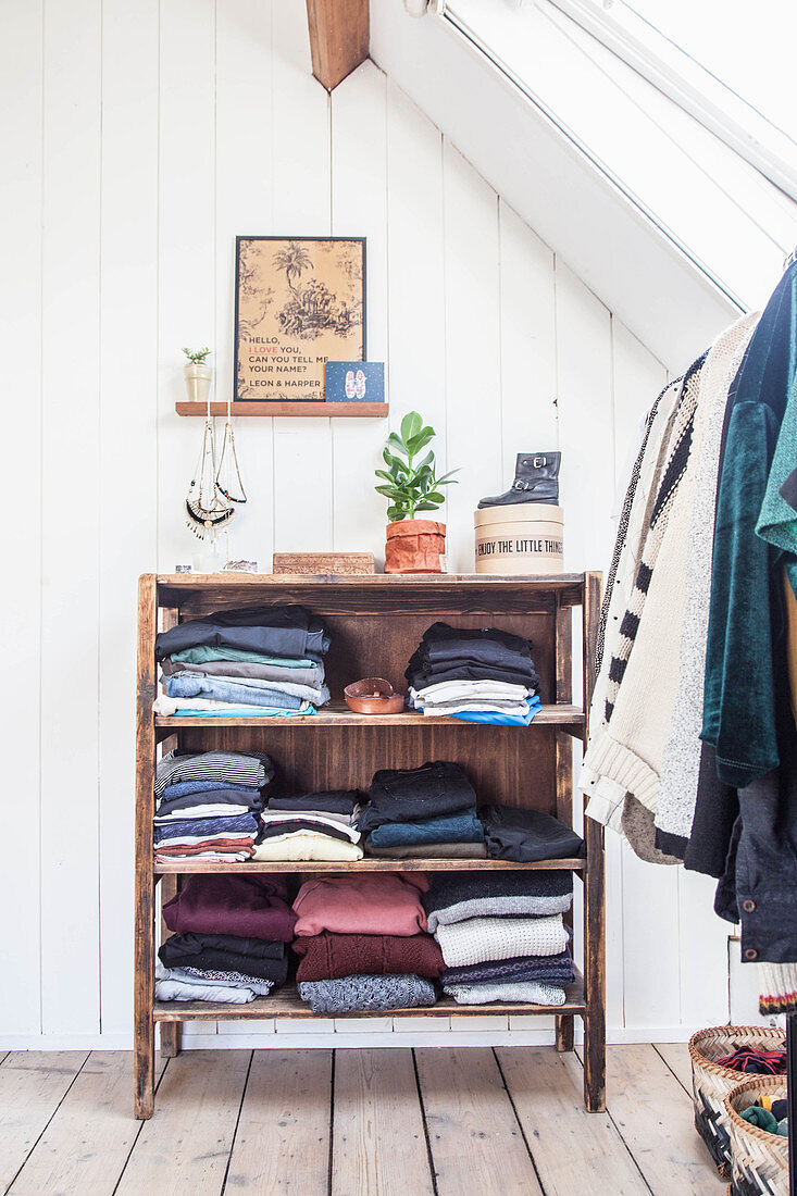 Folded clothing on open-fronted shelves and clothes rail in attic room with wooden floorboards