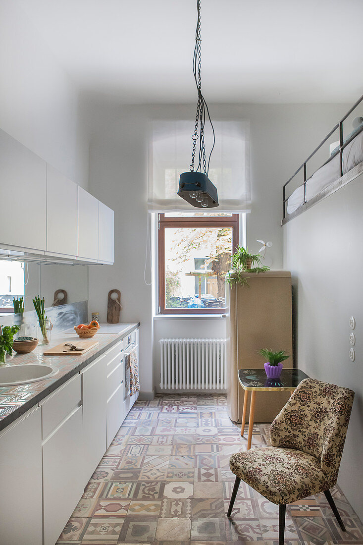 weiße Küchenzeile, ein Polsterstuhl und Kühlschrank in der Küche mit Galerie
