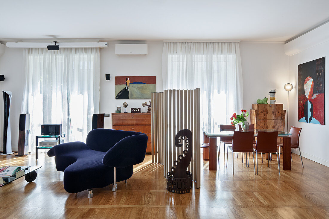 Designersofa und Essbereich, geteilt durch Paravent aus Pappröhren in offenem Wohnraum