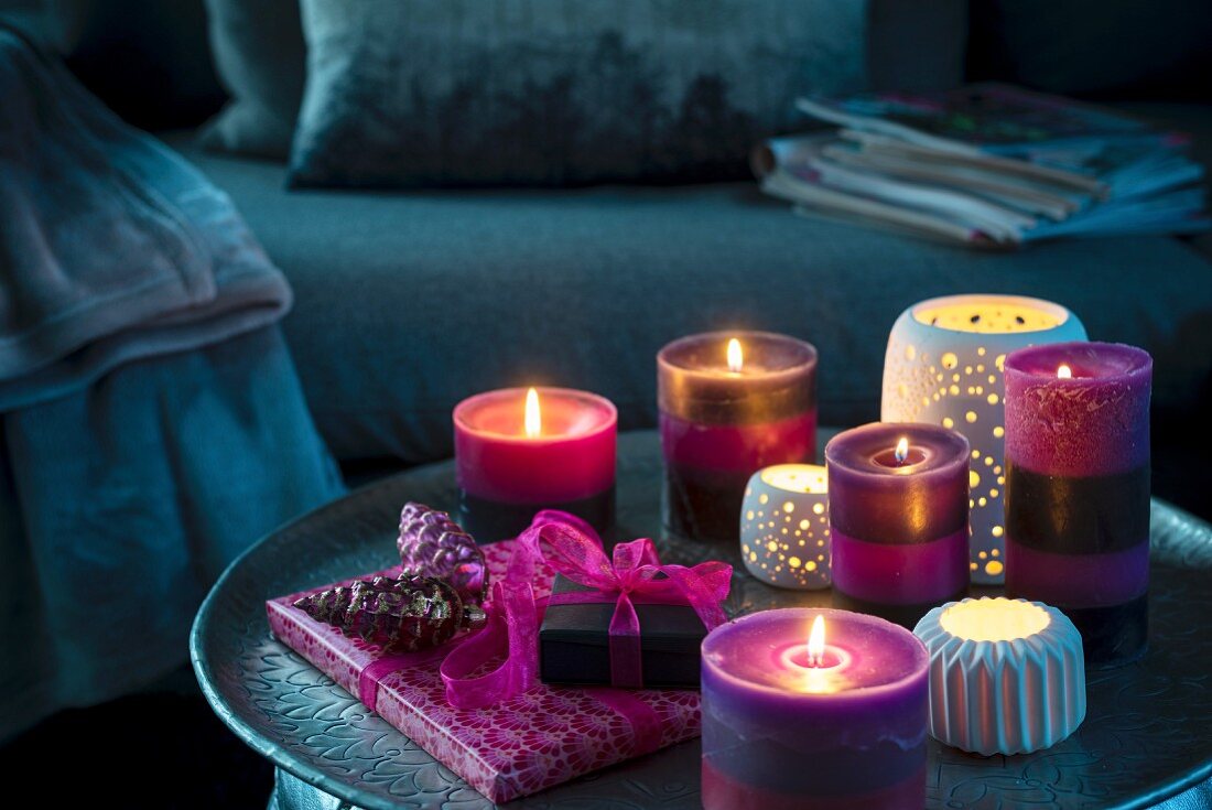 Violette Kerzen, Windlichter und Geschenke auf dunklem Couchtisch