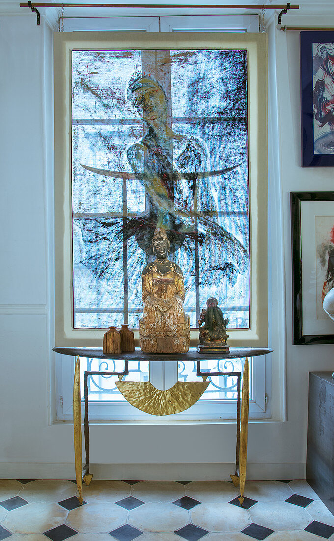 Buddha figurine on console table in front of window with painted translucent roller blind
