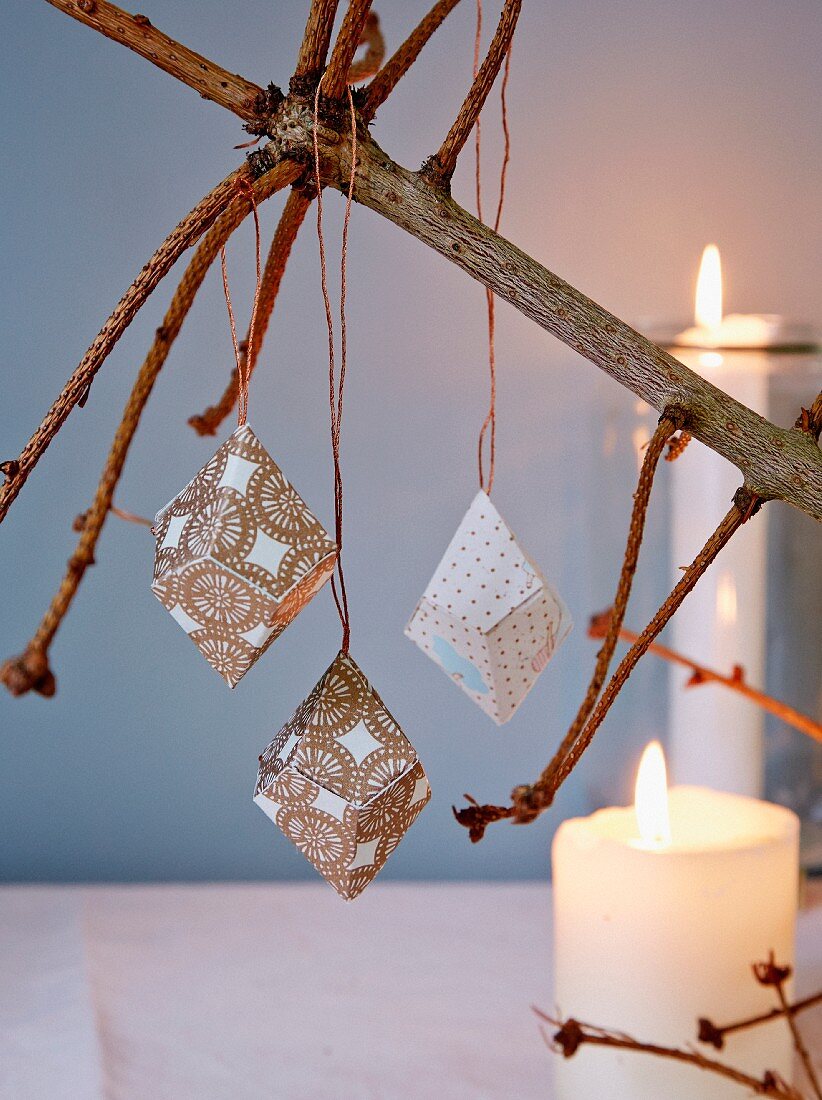 Paper prisms hung from naked fir branch in candlelight