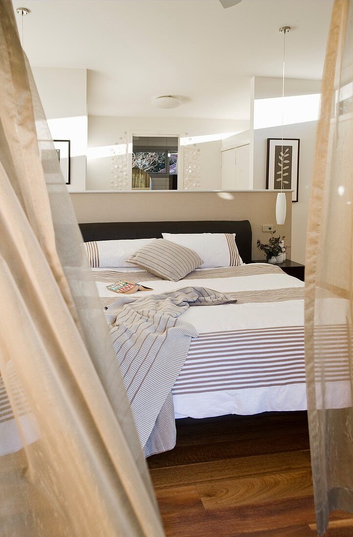 Blick ins Schlafzimmer auf Doppelbett vor halbhoher Brüstungsmauer als Raumteiler