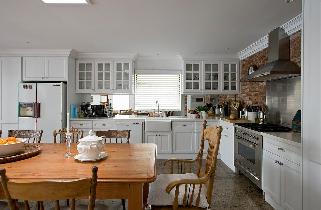Küche mit weißen Schrankfronten, im Vordergrund Esstisch aus Massivholz mit Stühlen
