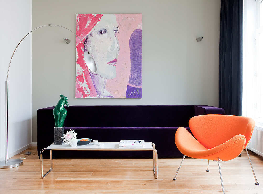 Orangefarbener Designersessel vor violettem Samtsofa im Wohnzimmer